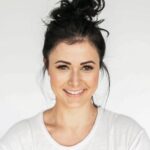 Headshot of a smiling woman with dark hair in a bun against a white background